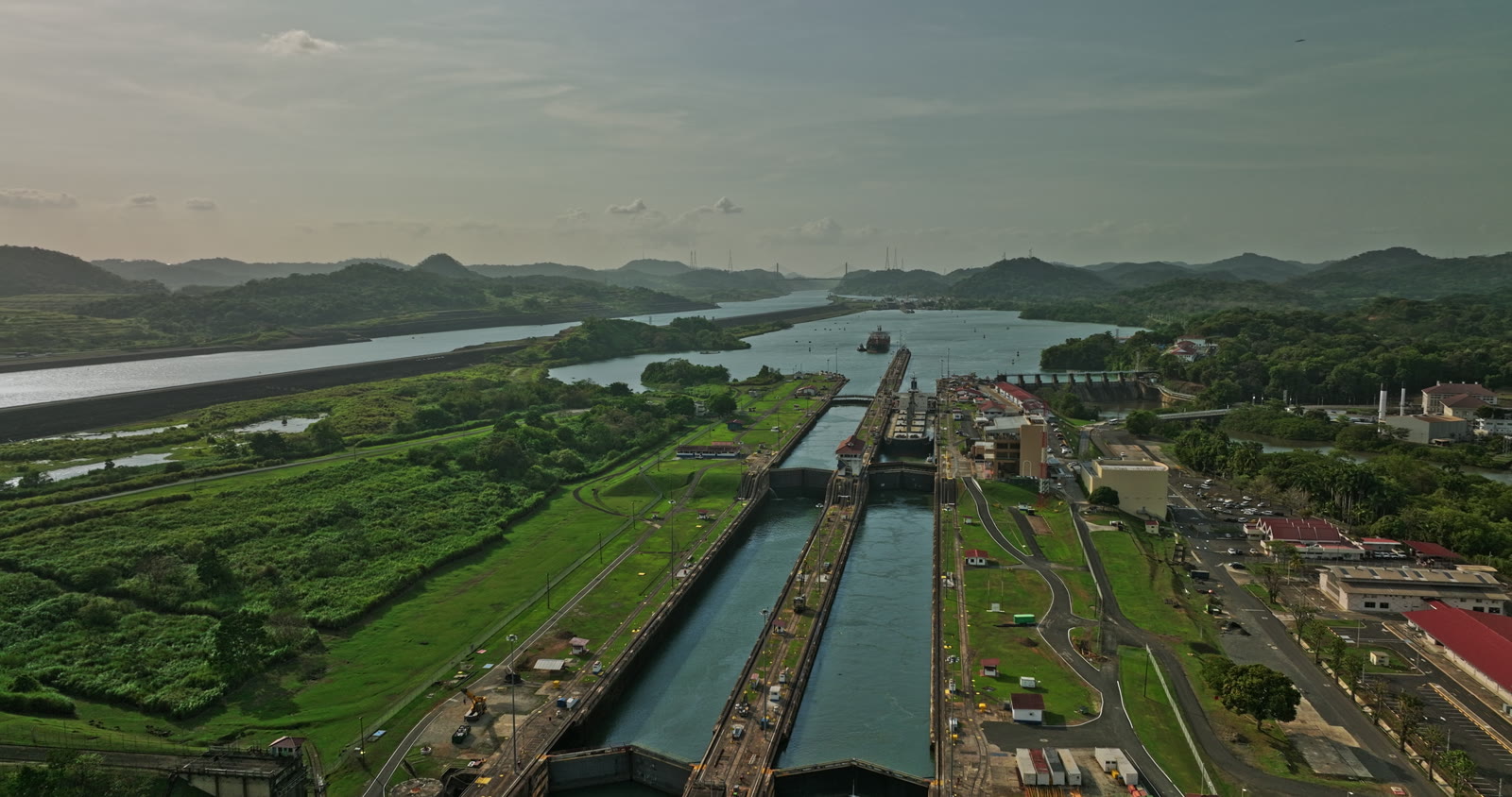 Vista aérea das eclusas do Canal do Panamá, com o canal seguindo entre as colinas ao fundo